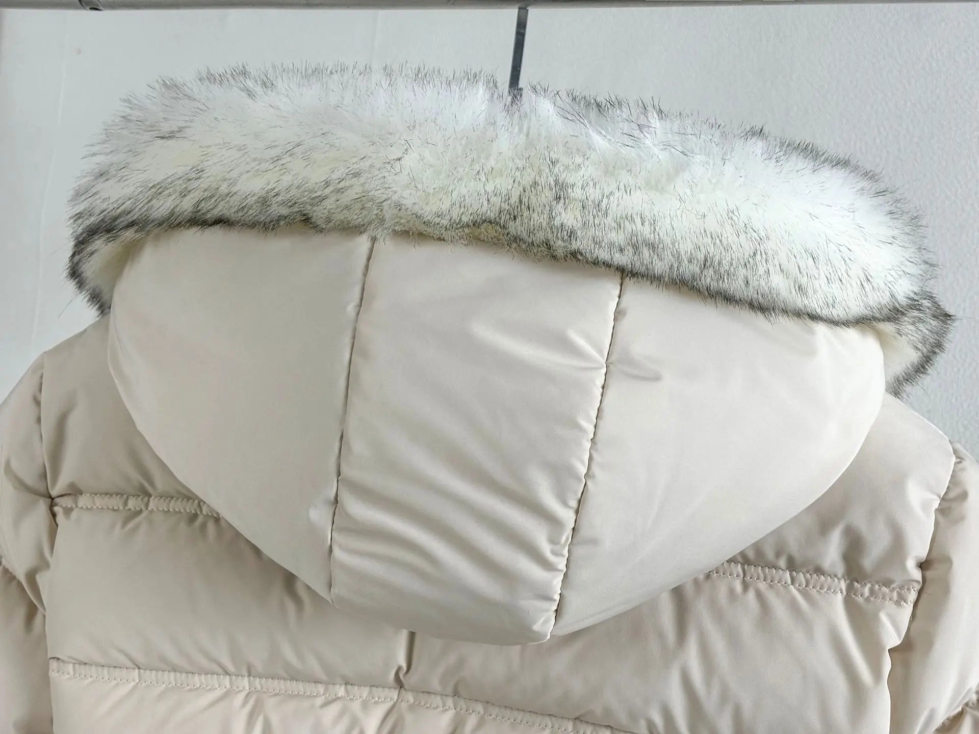 Beige puffer jacket with a fur-lined hood on a light gray background