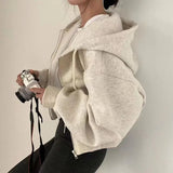 Person wearing a beige hoodie holding a camera against a plain background