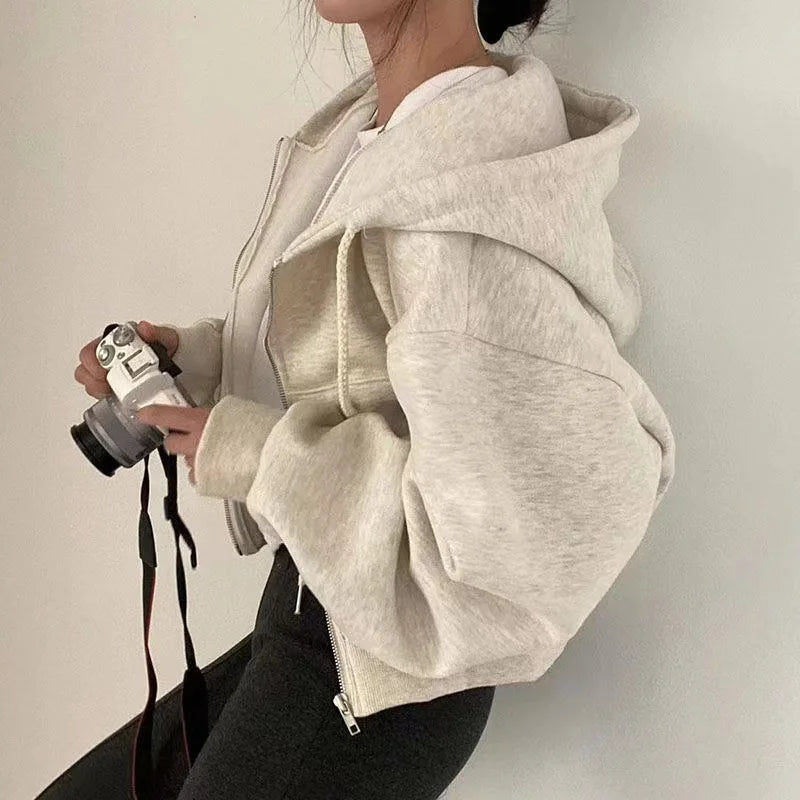 Person wearing a beige hoodie holding a camera against a plain background