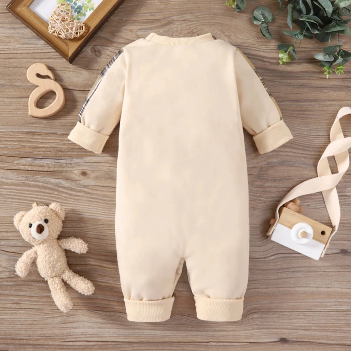 Beige baby romper on a wooden surface with a teddy bear and decorative items.