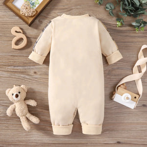 Beige baby romper on a wooden surface with a teddy bear and decorative items.