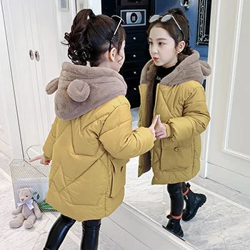 Two children wearing yellow puffer jackets with brown hoods in a room.