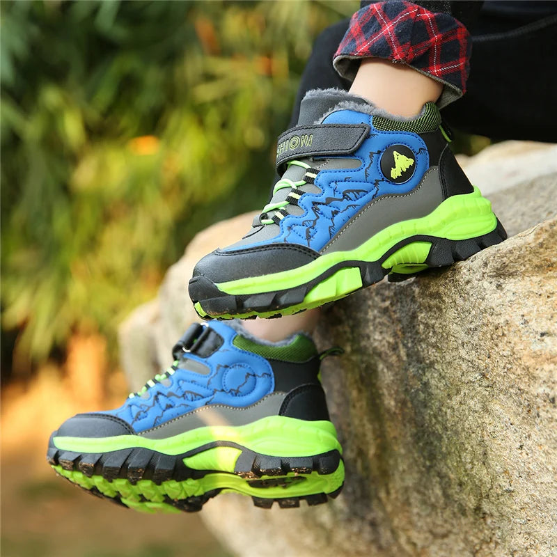 Child wearing blue and green hiking boots on a rock with a blurred natural background