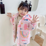 Child wearing a colorful pink jacket with rainbow patterns, standing indoors.