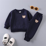 Navy blue children's outfit with bear embroidery, white sneakers, and sunglasses on a gray background