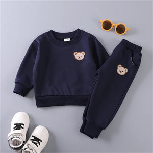 Navy blue children's outfit with bear embroidery, white sneakers, and sunglasses on a gray background